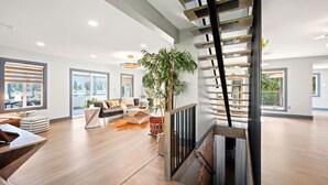 A spacious living area with a modern staircase, large windows, and a central plant.