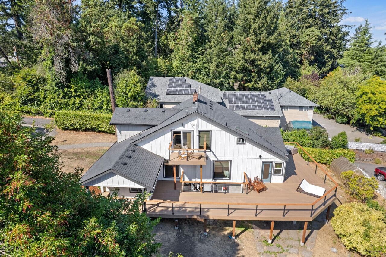 A two-story house with a deck, surrounded by dense forest.