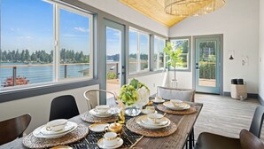 A dining area with a view of a lake and forest, large windows, and a wooden ceiling.