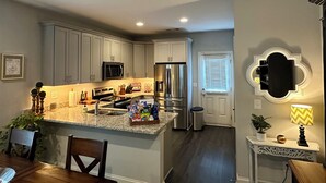 A modern kitchen with granite countertops, stainless steel appliances, and a central island. - Auburn Gameday Townhome (Opelika)