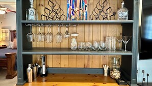 A bar area with shelves holding various glassware and bottles. - Auburn Gameday Townhome (Opelika)