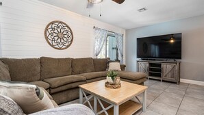 Un salon comprenant un canapé d’angle, une table basse en bois, un téléviseur à écran plat et un élément décoratif mural.