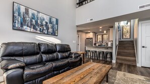 Un salon moderne avec un canapé en cuir noir, une table basse en bois et un tableau représentant un paysage urbain accroché au mur.