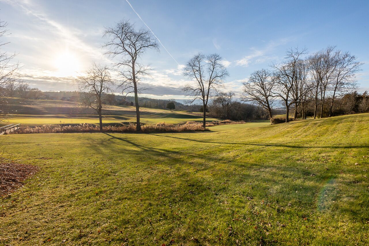 Un campo de golf con amplias zonas verdes, árboles y cielo despejado.