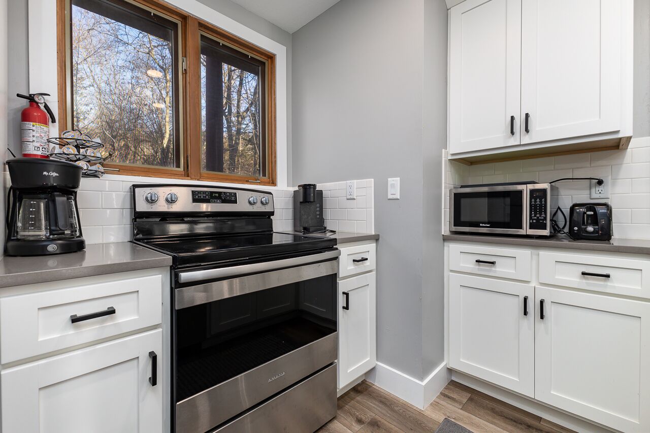 A modern kitchen with white cabinets, a stainless steel stove, a microwave, and a coffee maker.