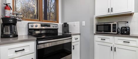 A modern kitchen with white cabinets, a stainless steel stove, a microwave, and a coffee maker.