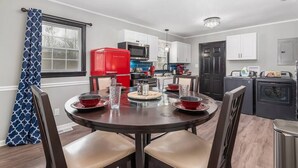 A modern kitchen with white cabinets, a red refrigerator, and a dining area with a round table and chairs. - "Crowder's Cottage" — Cozy retreat near Kings Mountain & Gastonia, NC (Gastonia)