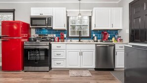 A modern kitchen with white cabinets, a red refrigerator, stainless steel appliances, and a blue tiled backsplash. - "Crowder's Cottage" — Cozy retreat near Kings Mountain & Gastonia, NC (Gastonia)