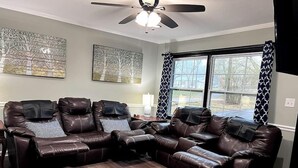 A living room with a sectional sofa, a ceiling fan, and large windows with patterned curtains. - "Crowder's Cottage" — Cozy retreat near Kings Mountain & Gastonia, NC (Gastonia)