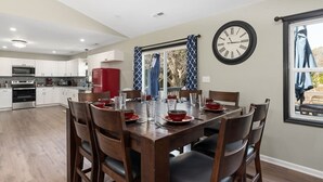 Une cuisine moderne avec des meubles blancs, un réfrigérateur rouge et un coin repas doté d’une table en bois, mise pour six personnes.