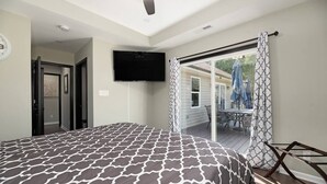 Une chambre dotée d’un grand lit, d’un ventilateur de plafond, d’un téléviseur fixé au mur et d’une porte-fenêtre coulissante donnant sur une terrasse extérieure.