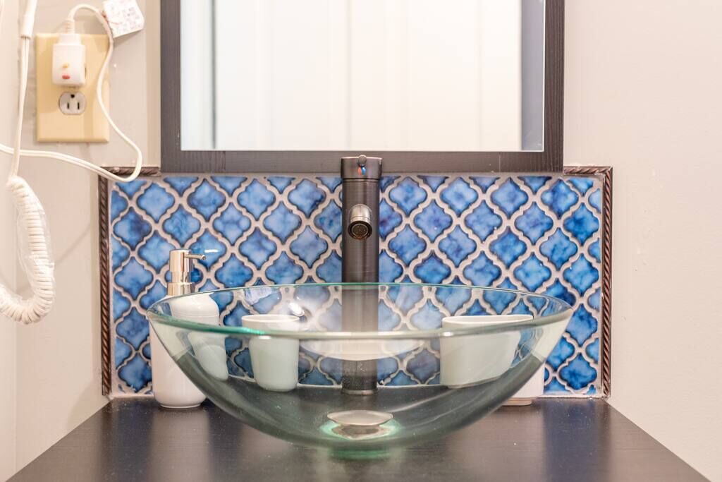 A bathroom with a glass bowl sink, a mirror above it, and a patterned blue tile backsplash.