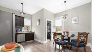 Una cocina moderna con armarios oscuros, encimera blanca y una zona de comedor con sillas de madera y mesa de vidrio.