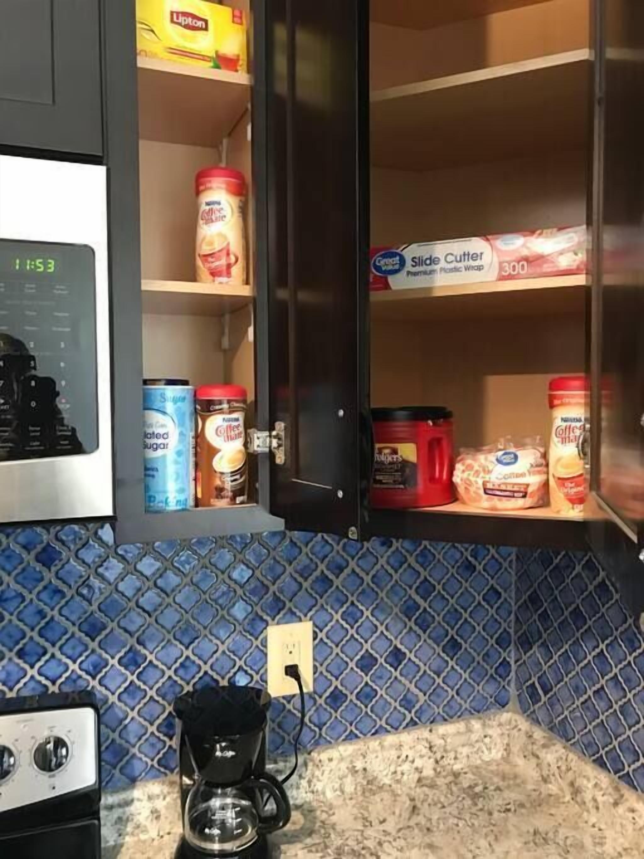 A kitchen with a coffee maker, a clock, and various food items on shelves.