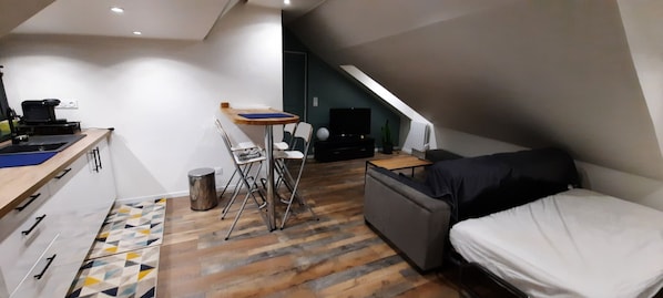 Ein kompakter Wohnraum mit Küchenzeile, klappbarem Esstisch, Sofa und Fernseher.