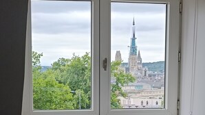 Et soveværelse med et vindue der kigger ud over bybilledet, en radiator og en seng med pude med et kortmønster.