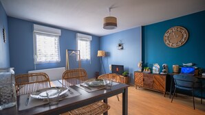 Uma sala de jantar com uma mesa de madeira posta para quatro pessoas, uma televisão e um relógio na parede.