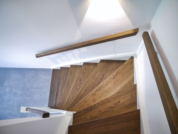 A staircase with wooden steps and white handrails, leading to a landing area with a light fixture.