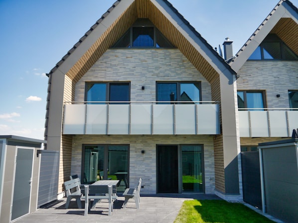 Une maison moderne à deux étages, dotée d’un balcon, de grandes fenêtres et d’une pelouse bien entretenue.