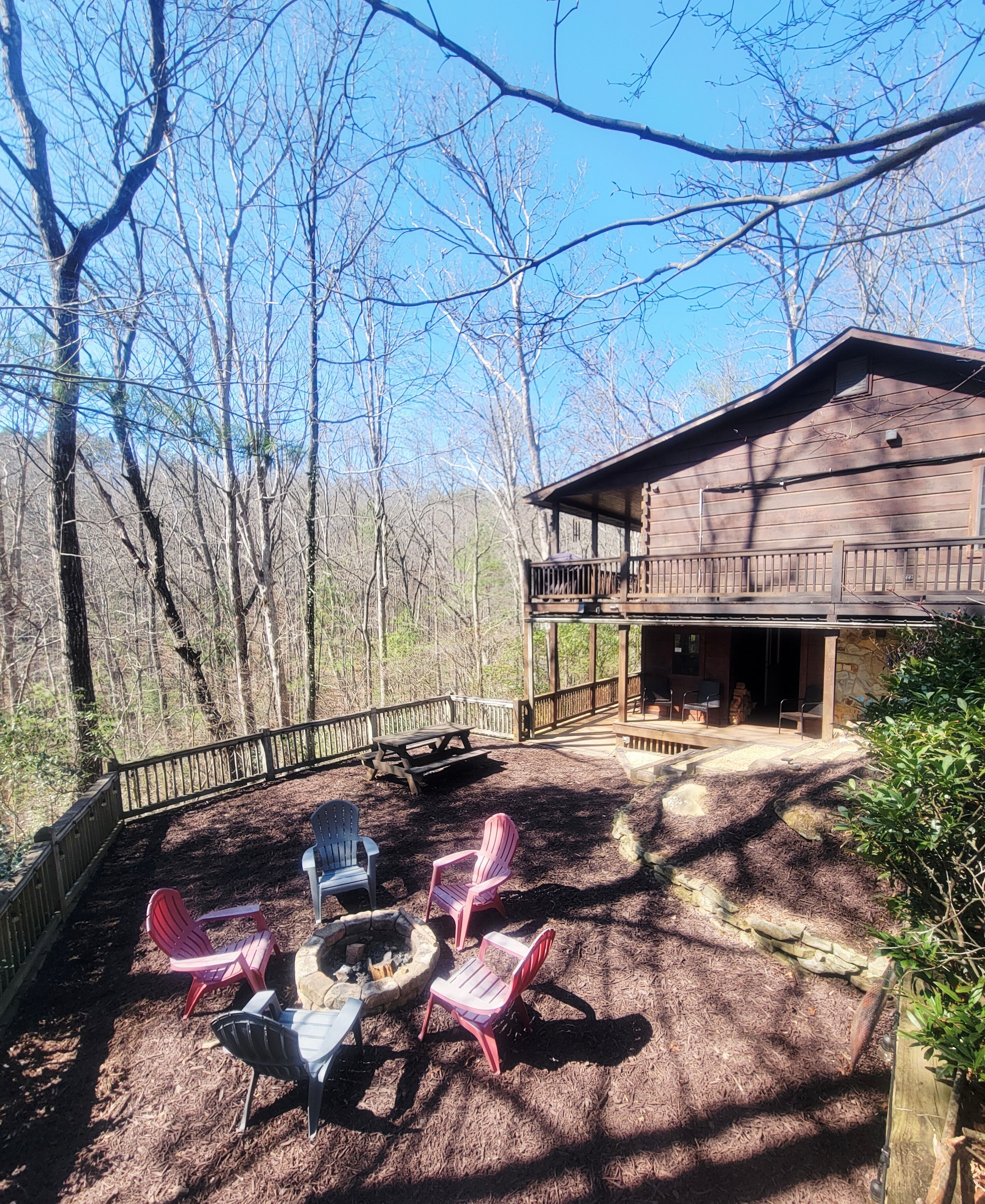 A wooden cabin with a deck, outdoor seating, and a fire pit.