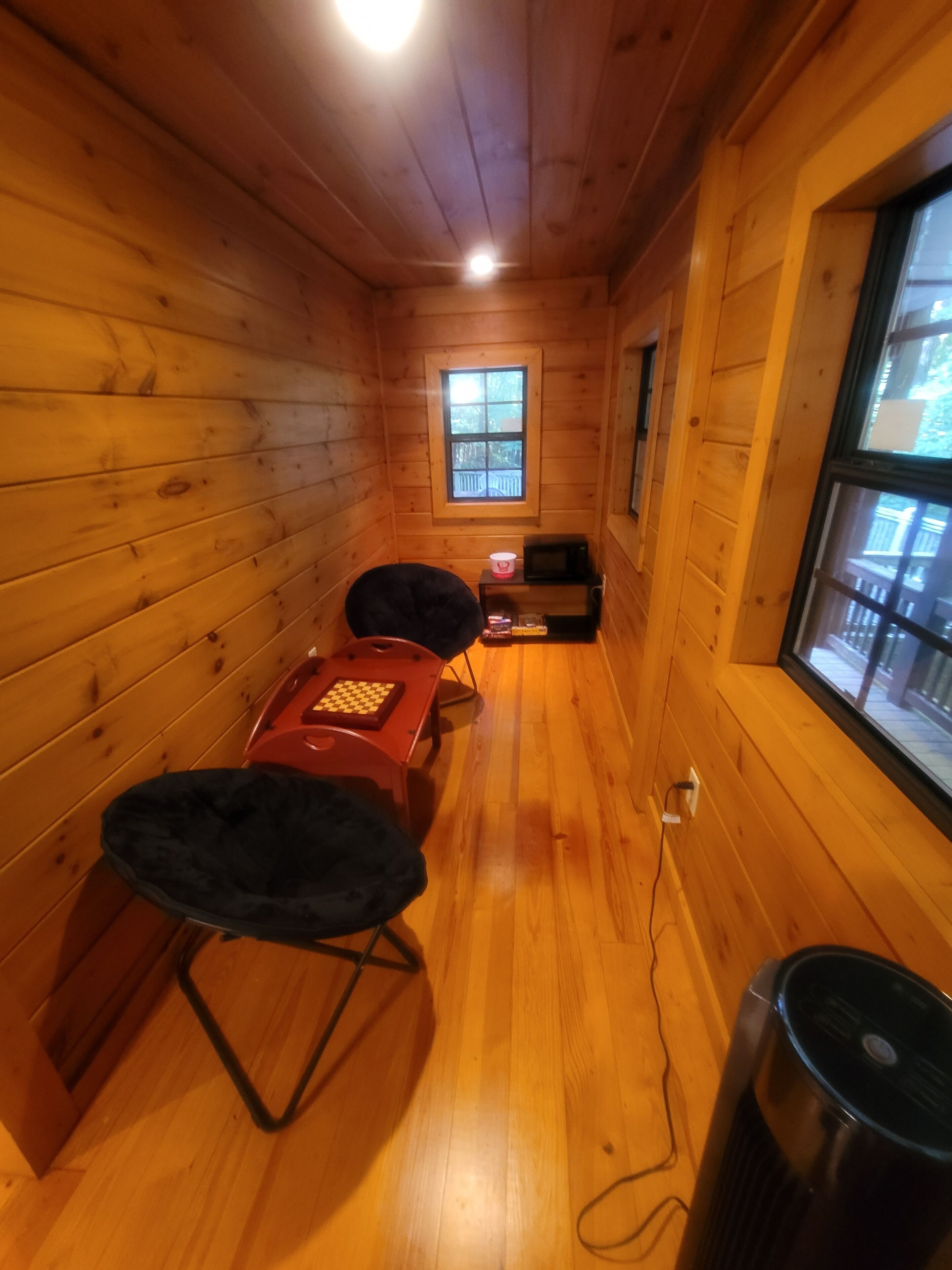 Une petite pièce en bois, avec une petite table, deux chaises, un four à micro-ondes et une fenêtre.