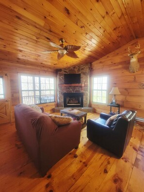 A wooden cabin interior with a stone fireplace, two sofas, a ceiling fan, and a mounted deer head. - Twin Fox Cabin Peaceful Blue Ridge/Ellijay Retreat (Cherry Log)
