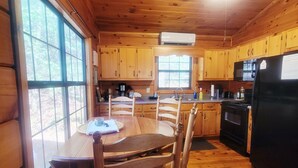 A wooden cabin interior with a dining table, chairs, a kitchen area with appliances, and large windows. - Twin Fox Cabin Peaceful Blue Ridge/Ellijay Retreat (Cherry Log)