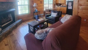 A cozy cabin interior with a fireplace, wooden walls, a ceiling fan, and a dining area. - Twin Fox Cabin Peaceful Blue Ridge/Ellijay Retreat (Cherry Log)