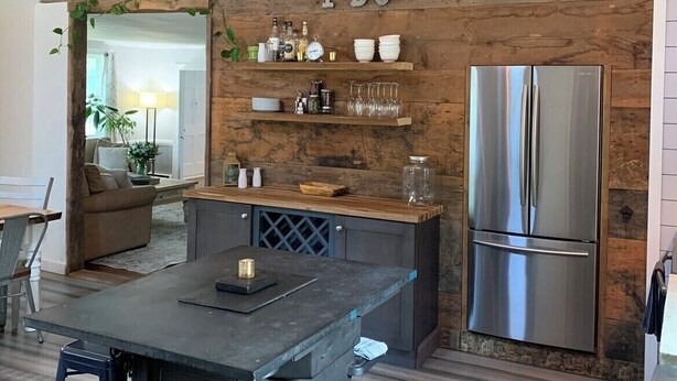 Une cuisine avec un mur en bois rustique, un réfrigérateur en acier inoxydable et une cuisinière encastrée.
