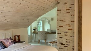 Une chambre avec un grand lit, un canapé gris, un plafond en bois et un mur décoré d’un motif en briques.