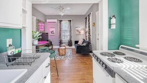 Une cuisine équipée d’une cuisinière, un coin repas avec une table et des chaises, et un salon avec un canapé et un ventilateur de plafond.