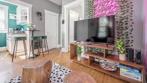 Un salon moderne avec un téléviseur à écran plat, une table basse en bois, des tabourets de bar et un néon mural.