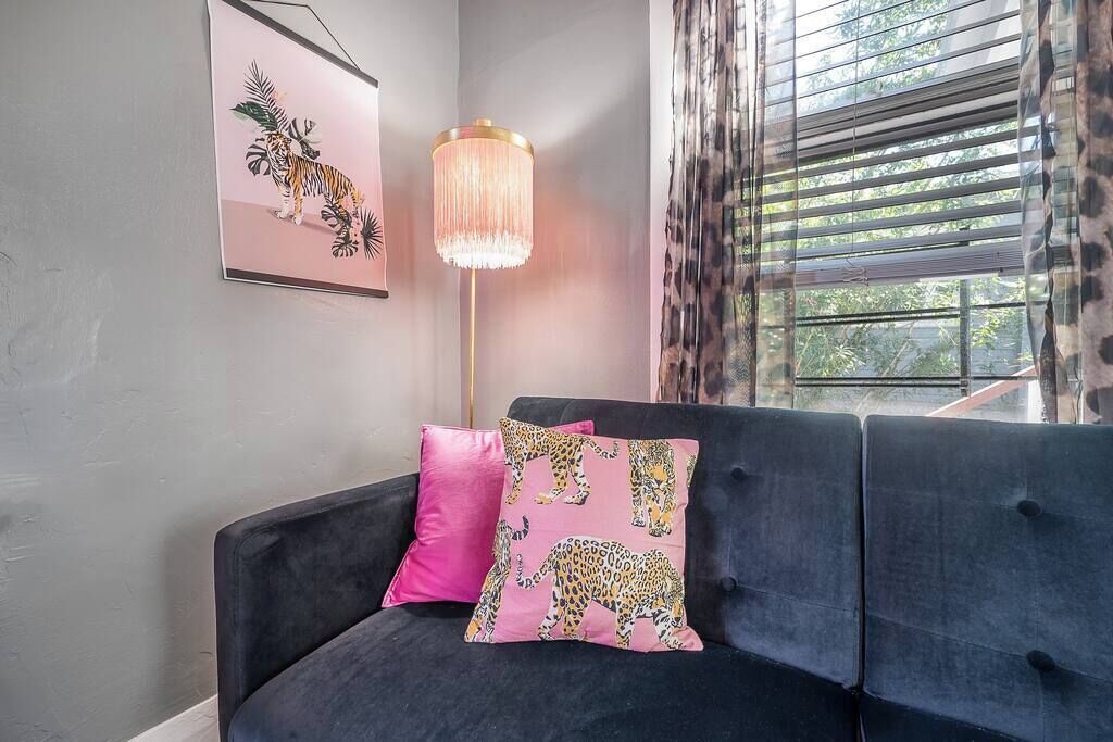 Un canapé de couleur sombre agrémenté de coussins à motifs léopard, un lampadaire et un tableau encadré accroché au mur.