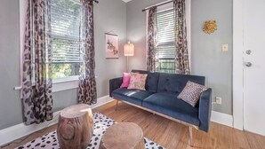Un salon avec un canapé bleu foncé, deux tabourets en bois, une lampe et des rideaux à motifs léopard.