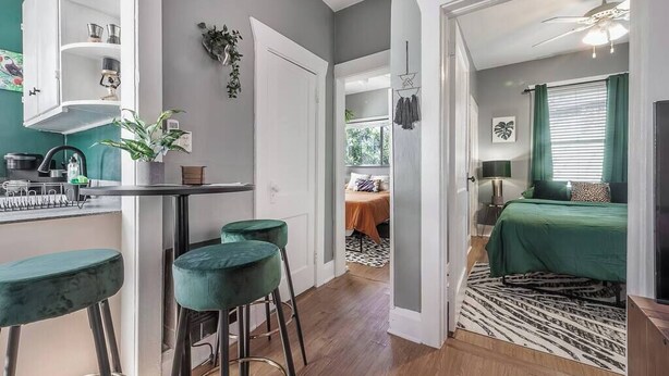 Un espace de vie compact comprenant un coin cuisine, un espace repas avec des tabourets de bar, une chambre avec une couvre-lit verte et un tapis à motifs.