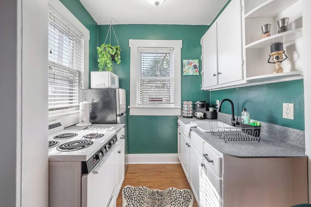 Una cocina compacta con armarios blancos, una estufa y una ventana con persianas.