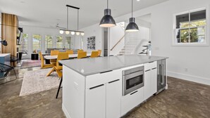 Cozinha moderna com ilha central, armários brancos, eletrodomésticos de aço inoxidável e iluminação pendente.