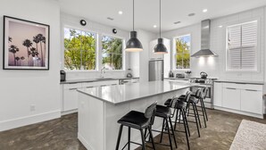 Cozinha moderna com uma ilha grande, banquetas, luminárias pendentes e vista para o exterior.