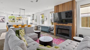 Uma sala de estar moderna com sofá, televisão de tela plana, lareira e área de jantar com cadeiras e mesa.