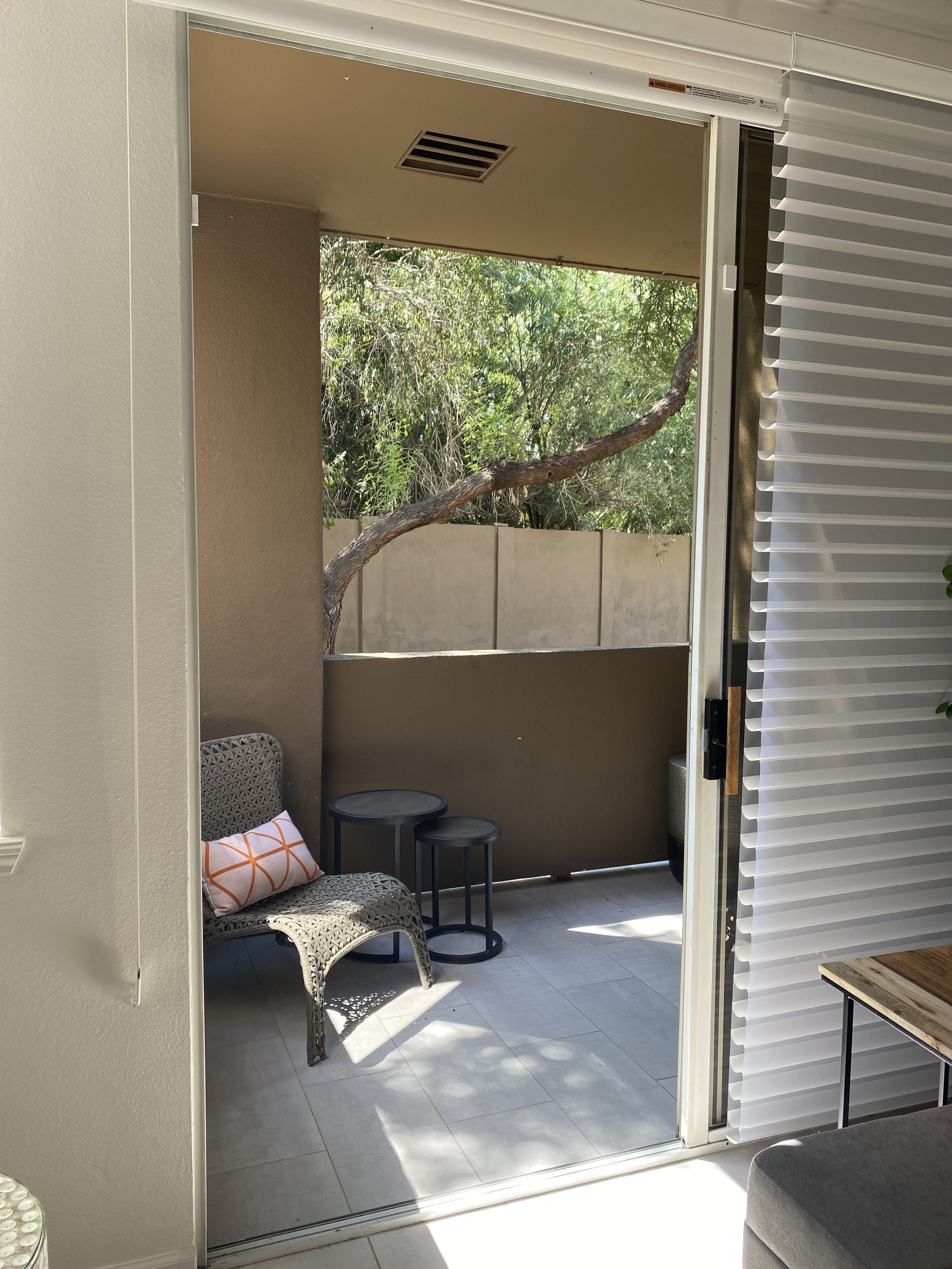 An open sliding glass door leading to an outdoor patio area with a chair, two small round tables, and a bench.