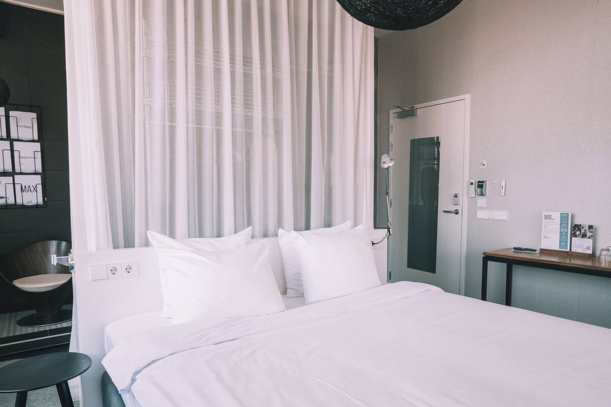 A hotel room with a bed, a chair, a desk, a shower, and a curtain.