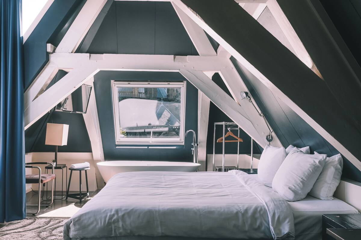 A bedroom with a large bed, a window, a bathtub, and a chair.