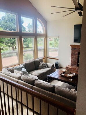 Relax in this inviting living room with a high ceiling, large windows, and a brick fireplace.