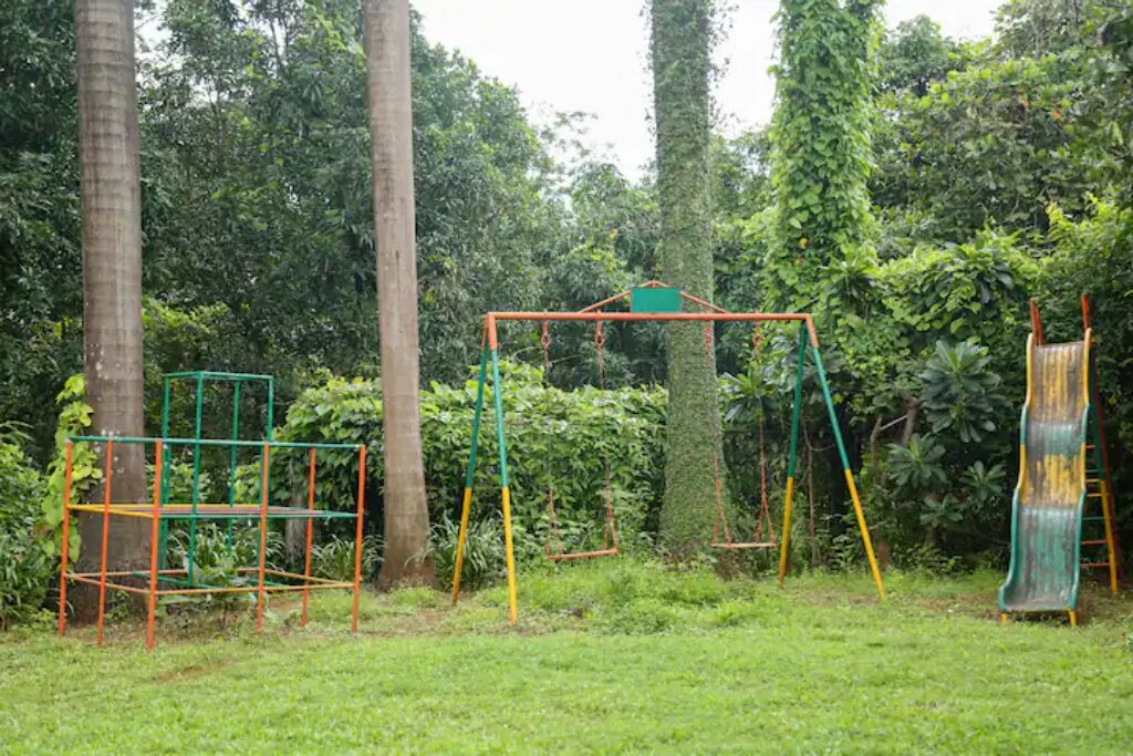 Un parque infantil con columpios y un tobogán, rodeado de árboles y follaje.