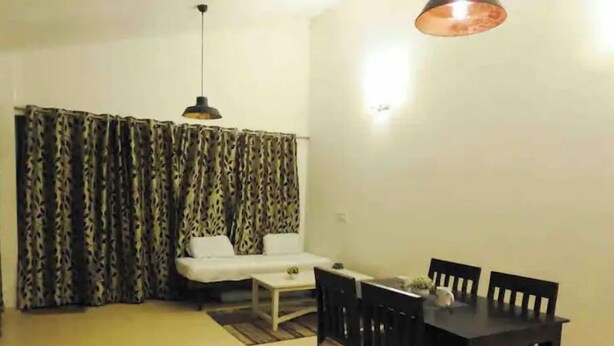 A living room with a sofa, a coffee table, a dining table with chairs, and a patterned curtain.