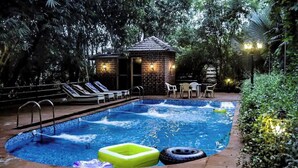 A swimming pool with lounge chairs and a small brick structure with lights. - LSQ RJ FARMS 3BHK VILLA WITH PRIVATE POOL! (Karjat)
