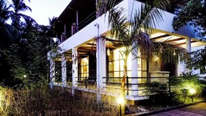 A modern building with a covered outdoor area, surrounded by vegetation. - LSQ RJ FARMS 3BHK VILLA WITH PRIVATE POOL! (Karjat)