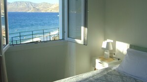 A bedroom with a view of the sea and mountains through a window.