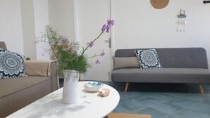 A living room with a grey sofa, a white coffee table, and a potted plant with purple flowers.
