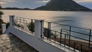 A balcony with a stone floor, a metal railing, and a view of a calm lake with a mountain in the background.